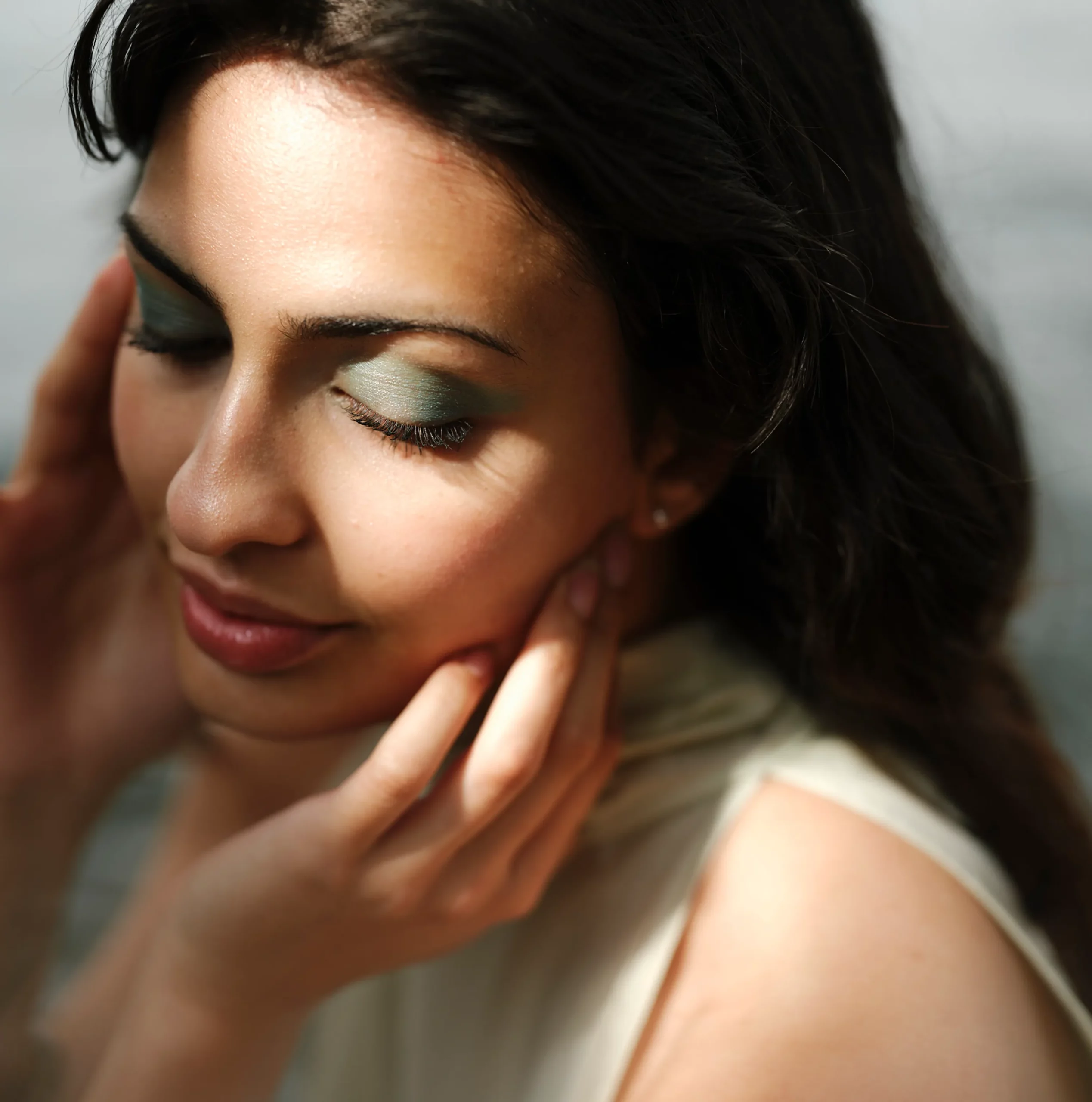 Gros plan d'une femme les yeux fermés se touchant le visage, mettant en valeur une peau lisse et éclatante après un traitement Julaine.